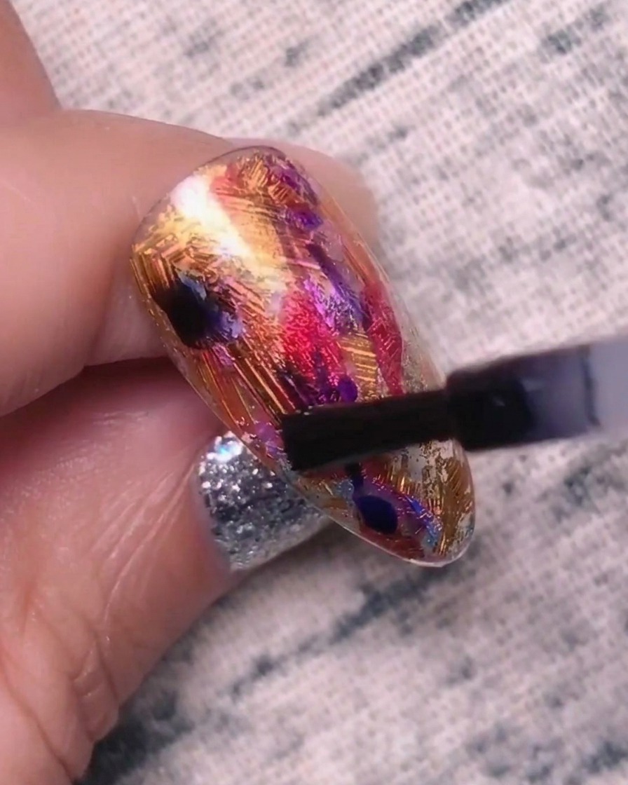Nahaufnahme eines Nagels, der mit blau-lila Gel betupft wird; man sieht, wie sich die Farben zu vermischen beginnen.