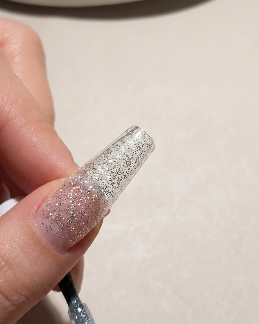 Nahaufnahme einer Nagelspitze, die mit silbernem Glitzer-Gel-Lack überzogen wird.