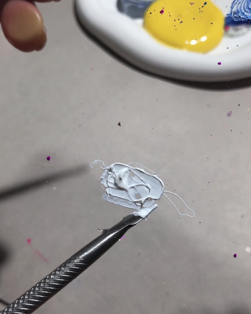 Nahaufnahme eines Mischwerkzeugs, das weißes Mal-Gel und Frucht-Gel zu einer glatten, cremigen Konsistenz vermengt.