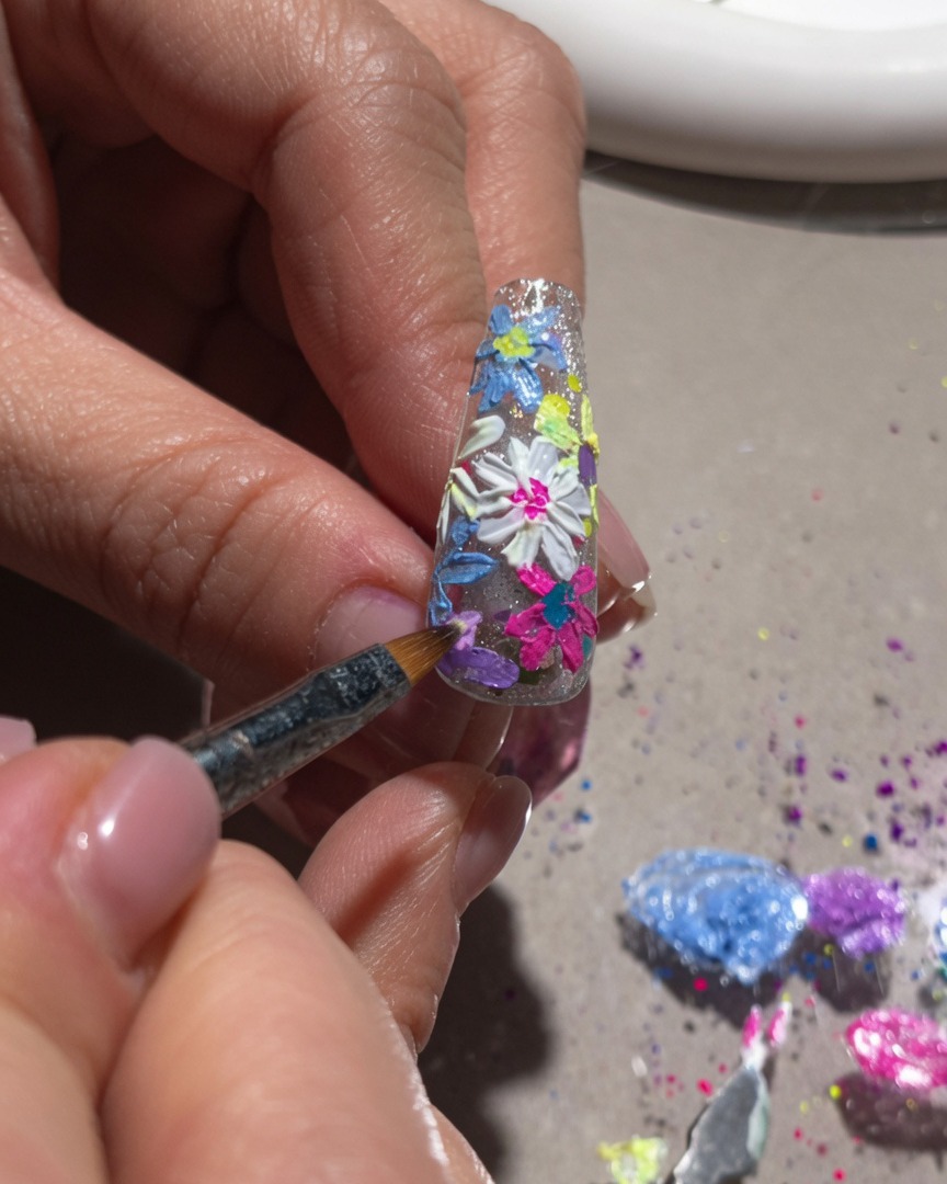 Nahaufnahme eines Fein-Pinsels, der weiße Highlights und mittlere Details zu einem 3D-Blumen-Nageldesign hinzufügt.