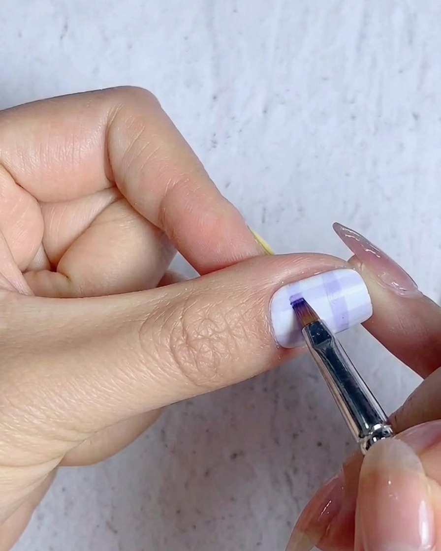 Ein feiner Pinsel füllt die Schnittpunkte des Gittermusters auf einem Karodesign mit blauem Gel.