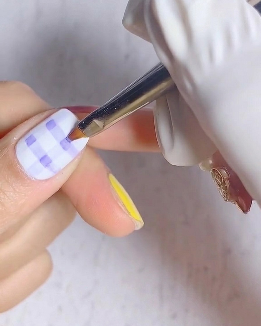 Eine Nahaufnahme eines Fingernagels mit blau-weißem Karomuster, der unter einer UV-Nagellampe liegt.