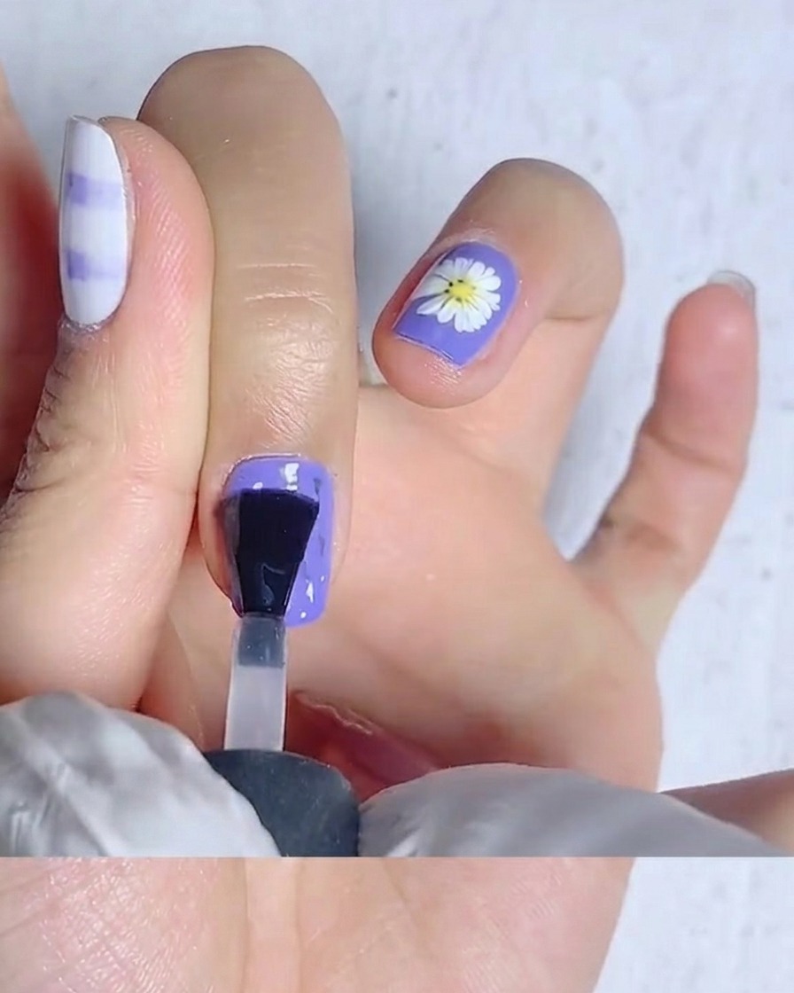Ein Nagelpinsel verteilt matten Überlack auf einem hellgelben Nagel.