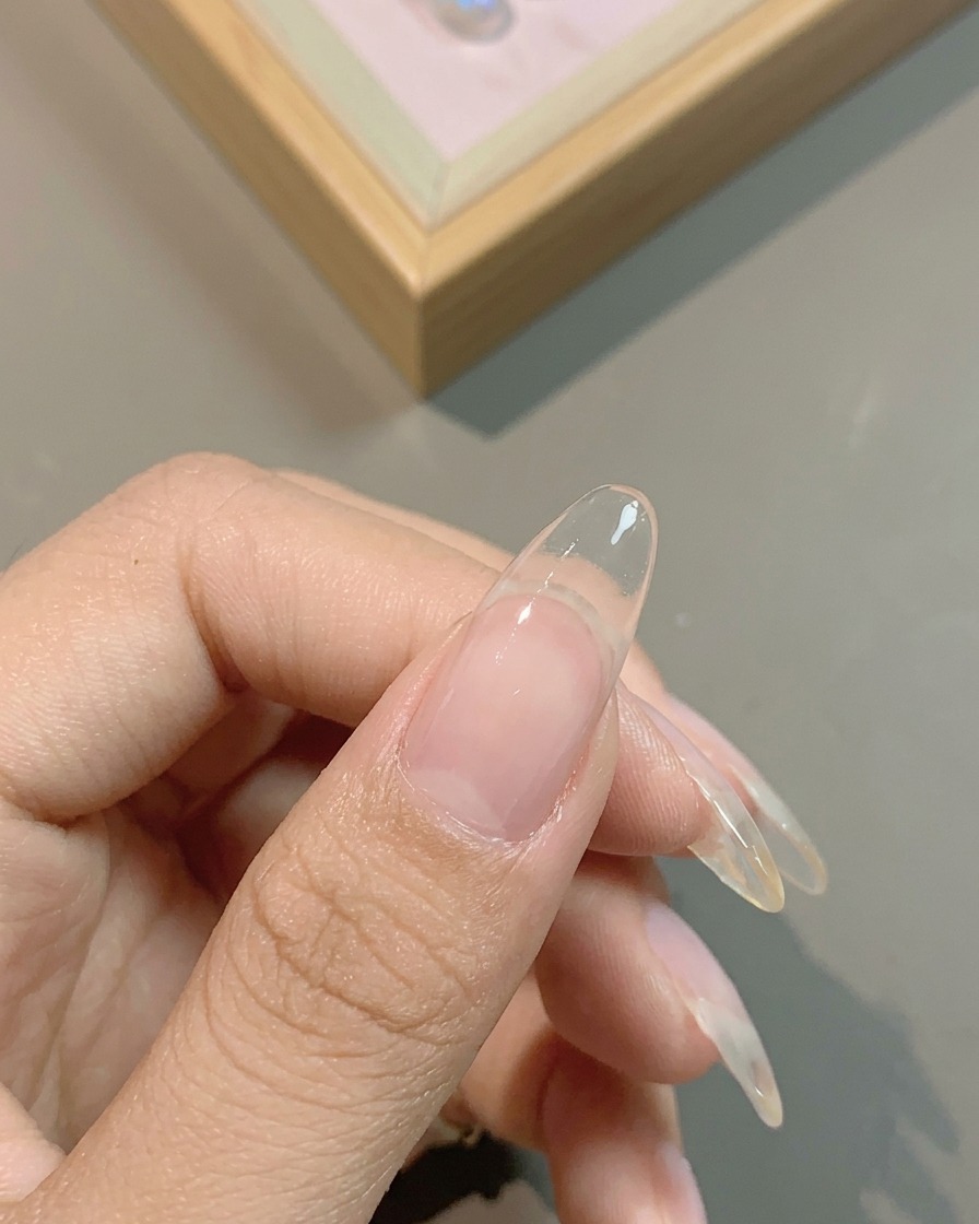 Ein Pinsel trägt eine durchscheinende, milchig-weiße Gel-Basis auf einen Fingernagel auf.