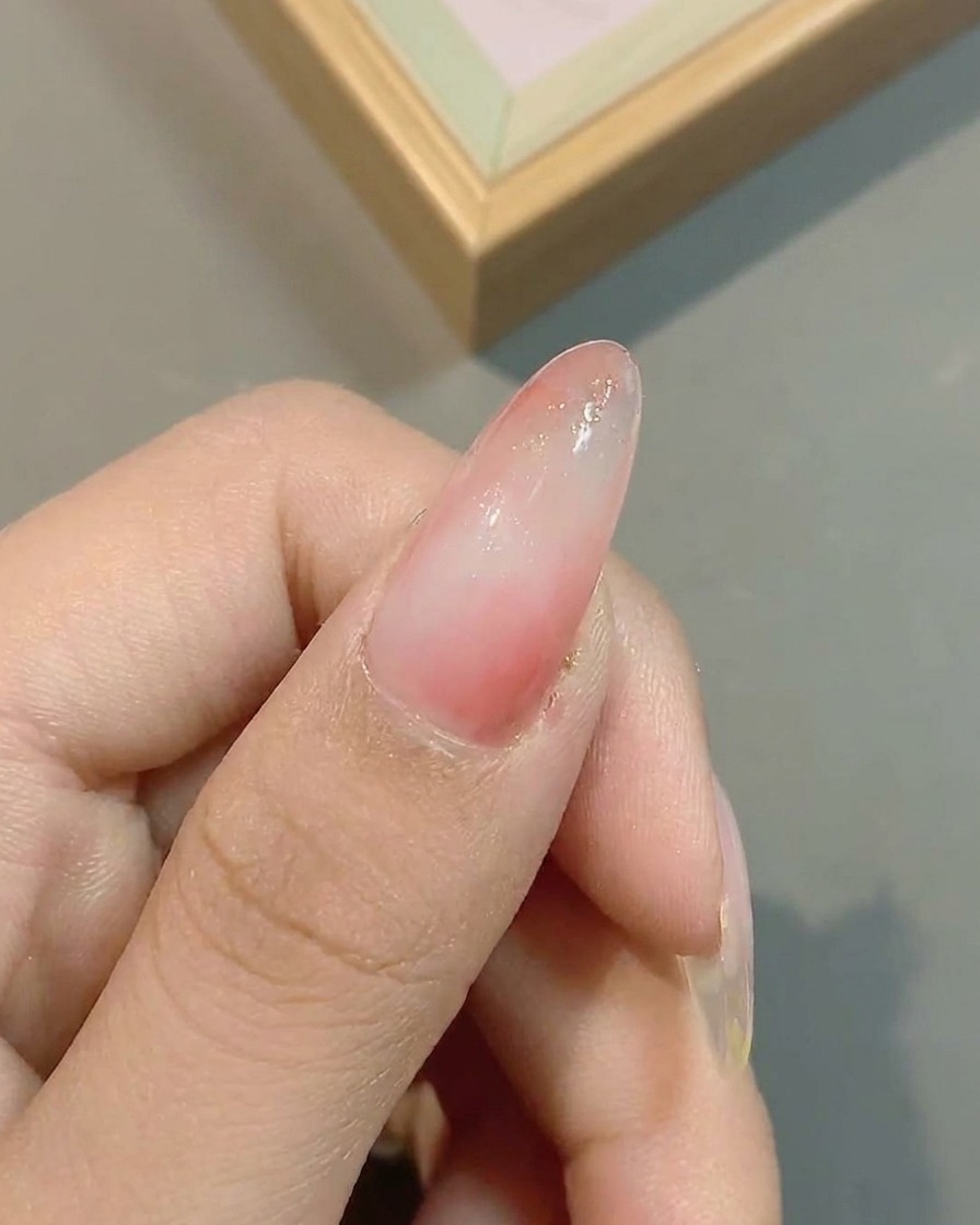 Glitzerpartikel werden über dem ausgehärteten rosa Ombré-Nagel verteilt.
