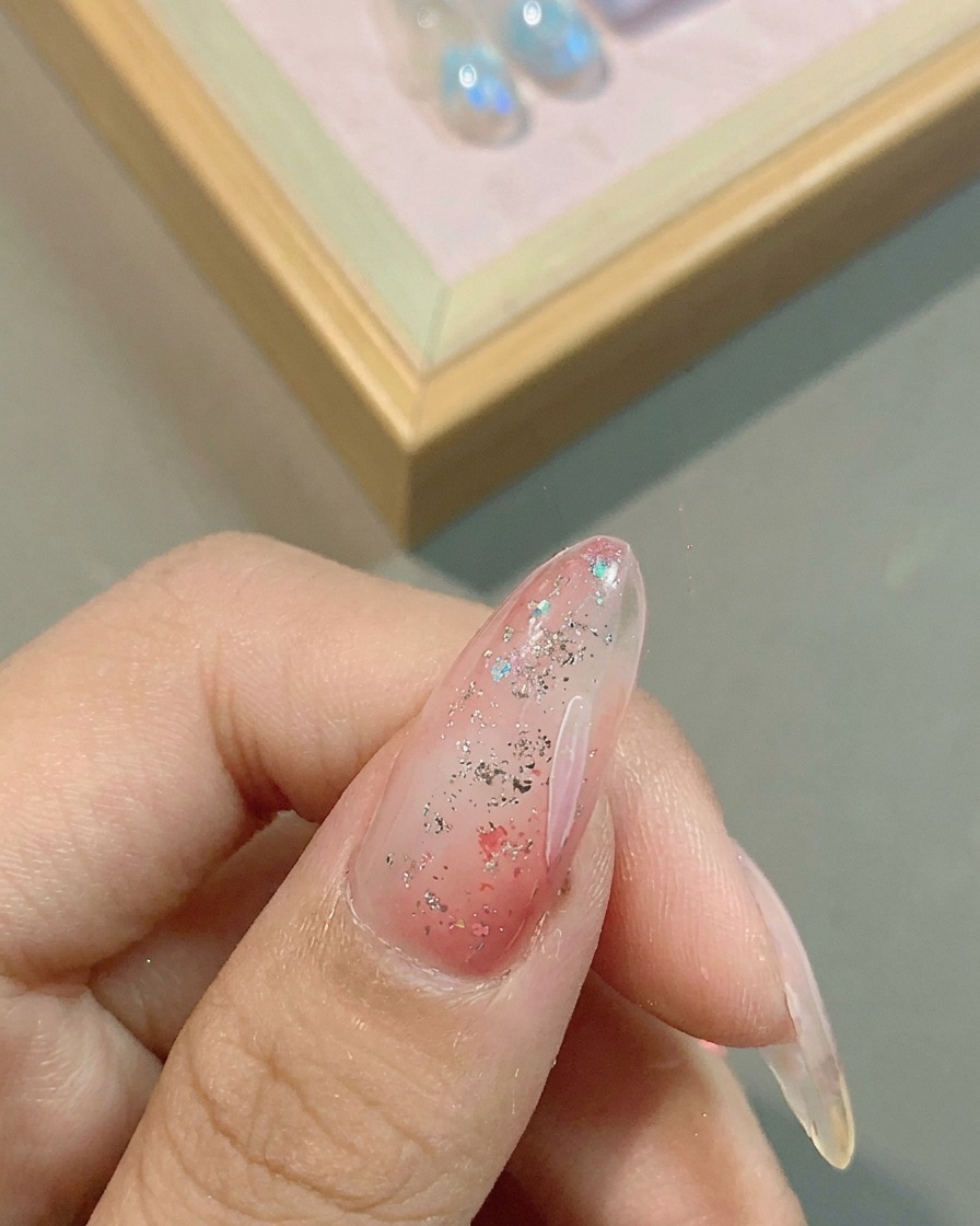 Ein feiner Liner-Pinsel zeichnet zarte weiße Blütenblätter auf eine rosa glitzernde Basis.