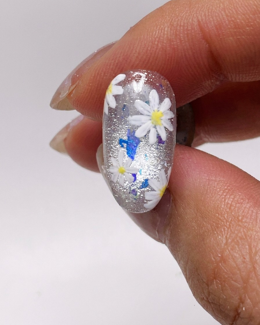 Ein Nagelpinsel trägt eine dünne Schicht silbernes Cat-Eye-Gel auf einen Naturnagel auf.