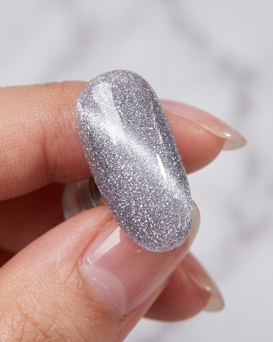 Ein Magnet wird über den nassen, silbernen Cat-Eye-Nagel gehalten, um einen schimmernden Lichtstreifen zu erzeugen.