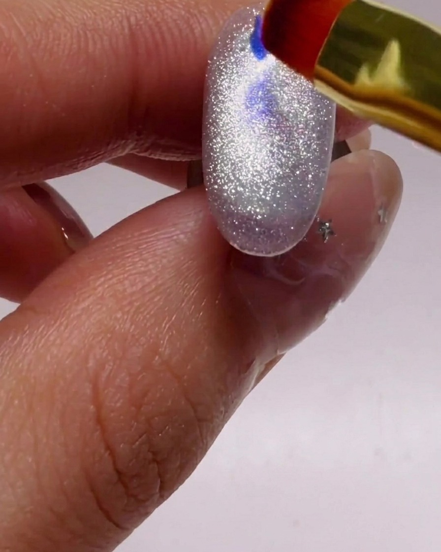 Ein kleiner Pinsel platziert blaue und violette Glitzer-Flakies auf dem schimmernden silbernen Untergrund.