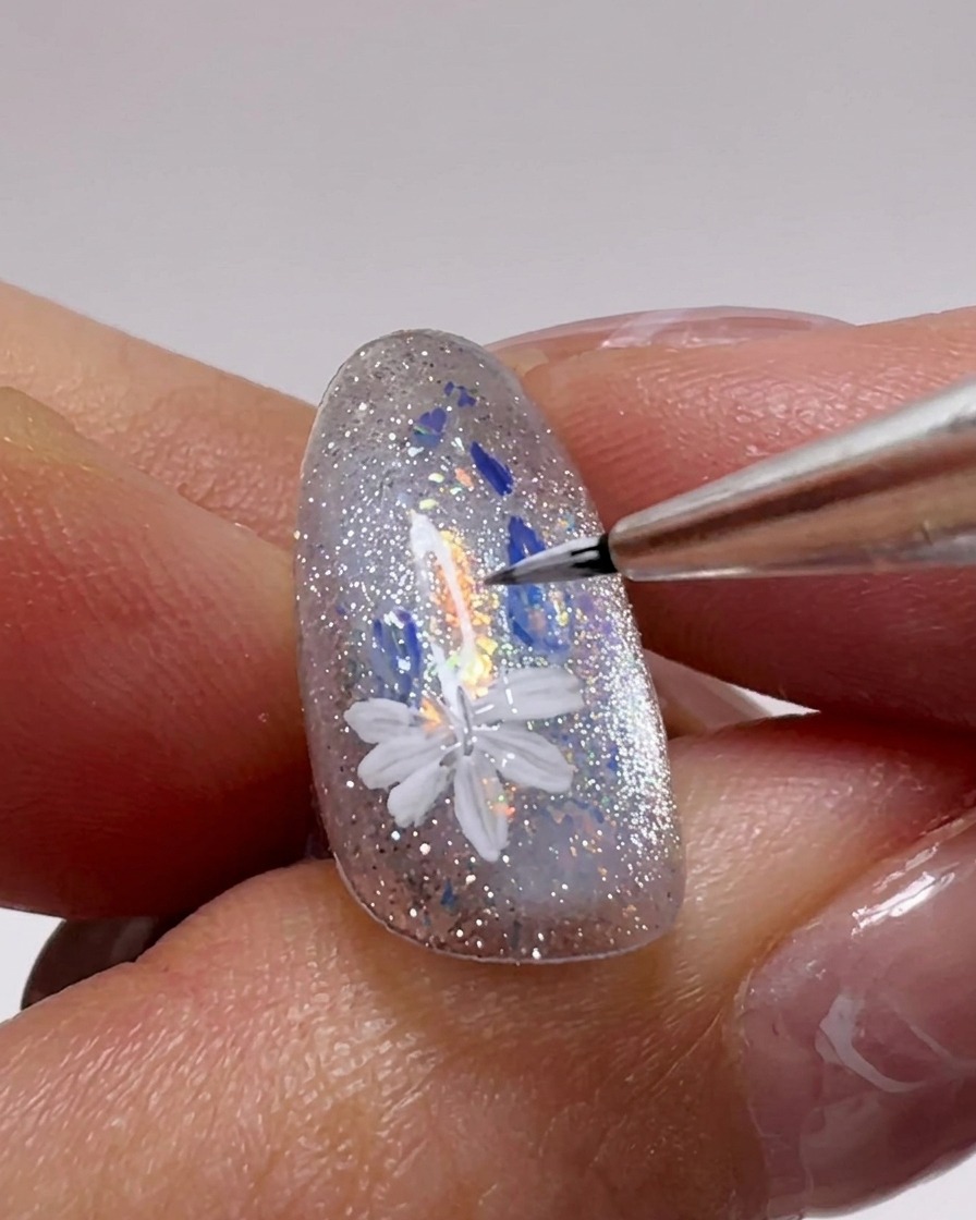 Nahaufnahme von weiteren weißen Gänseblümchen, die mit einem Detailpinsel auf den Nagel gemalt werden.