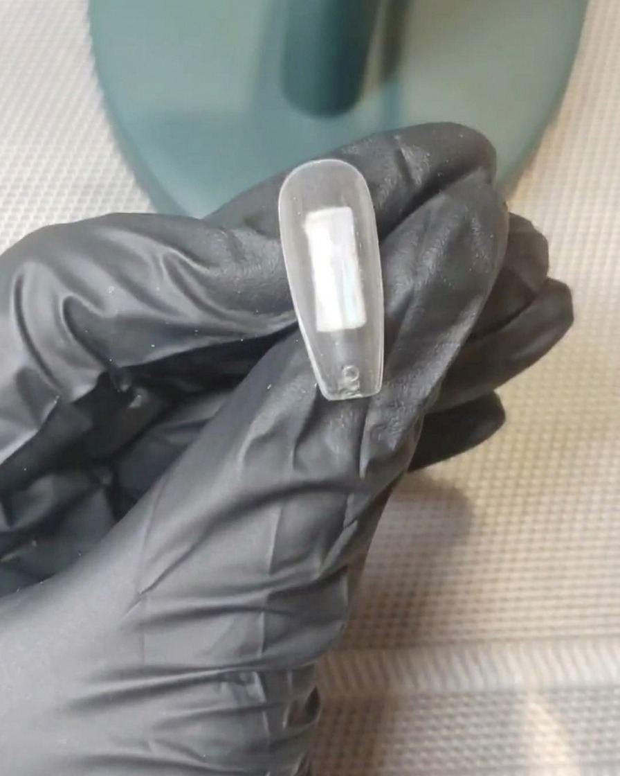 Nahaufnahme einer klaren Nagelspitze mit deutlichen Punkten aus nudefarbenem Rosa und milchig-weißem Gel in der Mitte.
