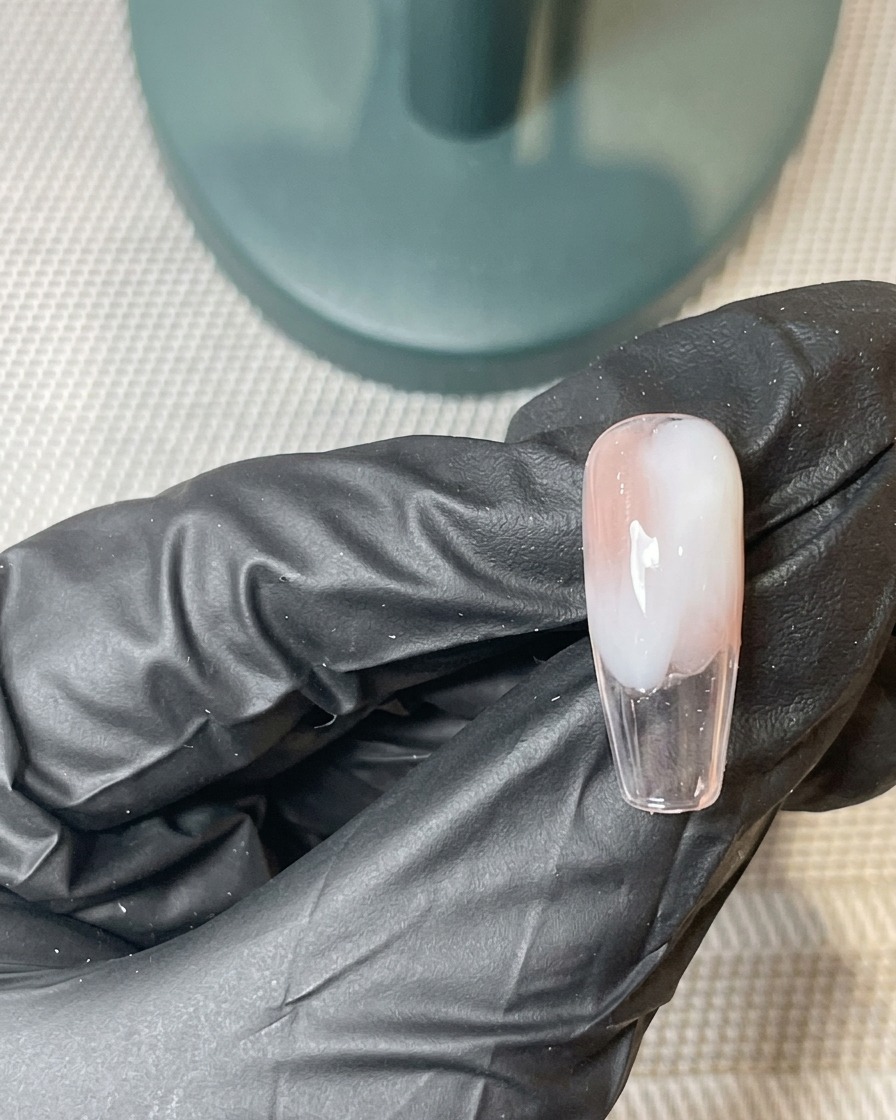 Ein Pinsel trägt eine zweite dünne Schicht rosa und weißes Gel über der ausgehärteten Ombré-Basis auf.