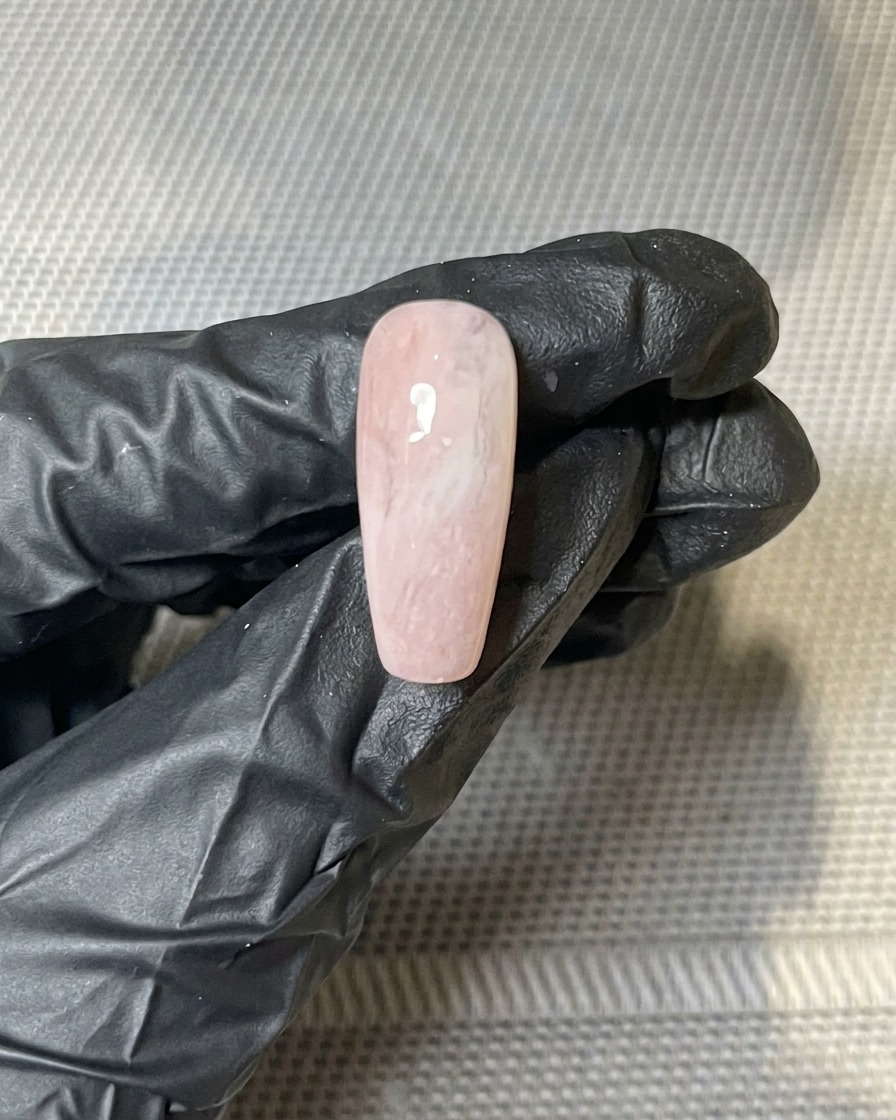 Nahaufnahme von Blattgold-Flocken, die auf die klebrige Oberfläche eines gel-lackierten Nagels gedrückt werden.
