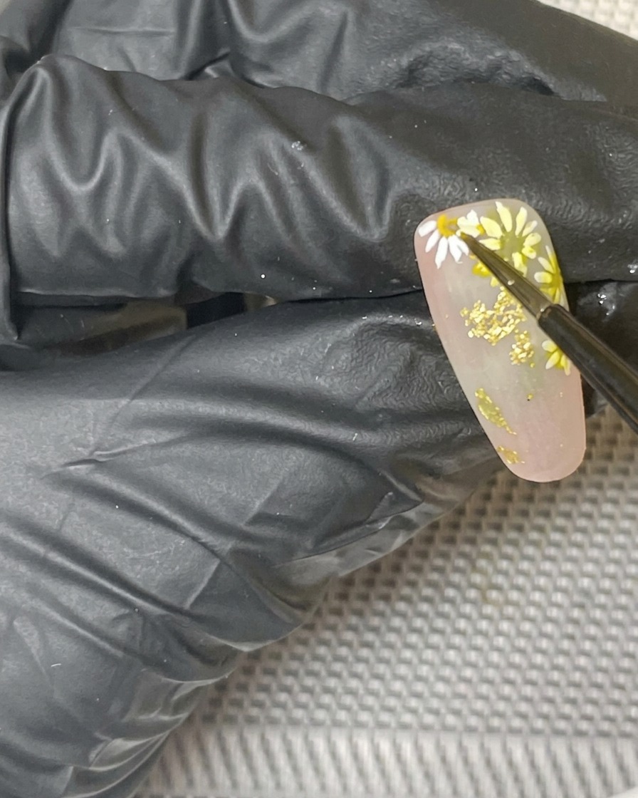 Nahaufnahme des fertigen Gänseblümchen-Nageldesigns, das in einer Lampe aushärtet.