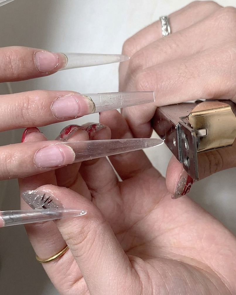 Ein Nagelpinsel verteilt eine Schicht klares Gel-Base-Coat am Übergangspunkt zwischen Naturnagel und Verlängerung.