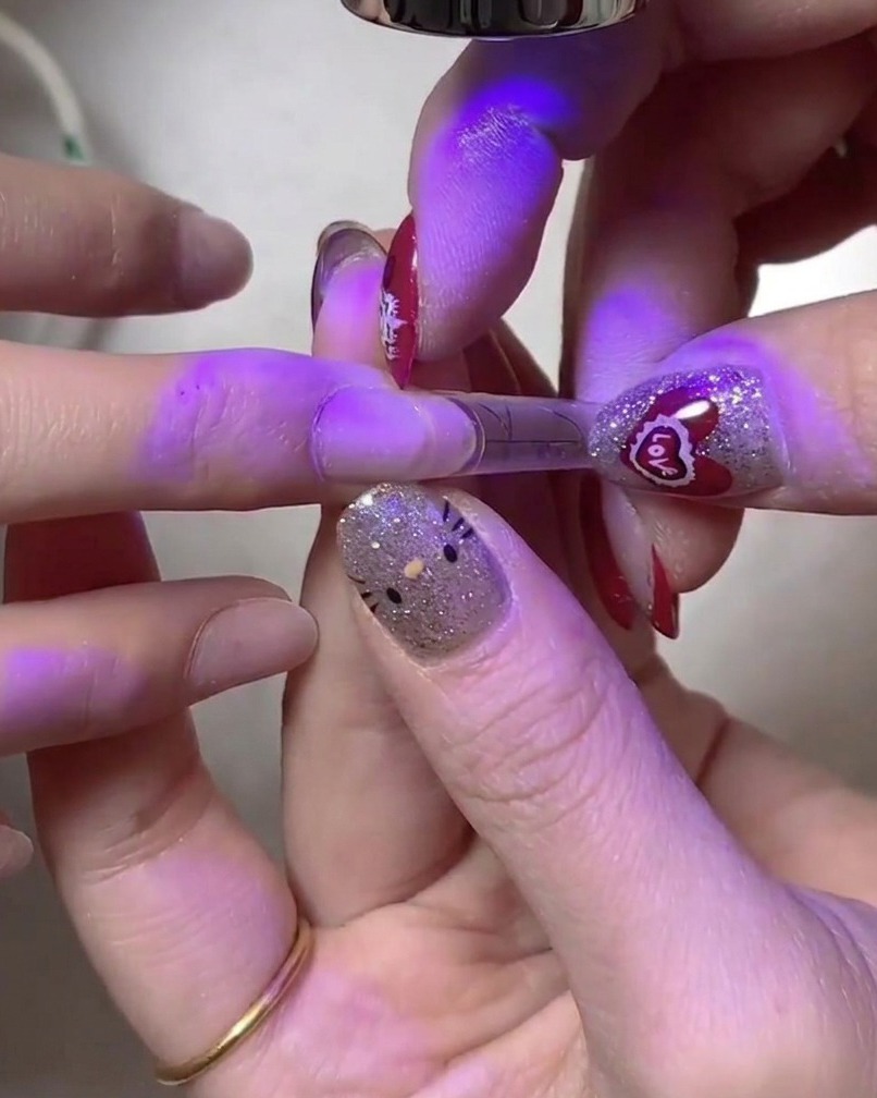 Eine Hand hält den Nagel unter einer zweiten UV/LED-Lampe für eine gründliche Härtung.