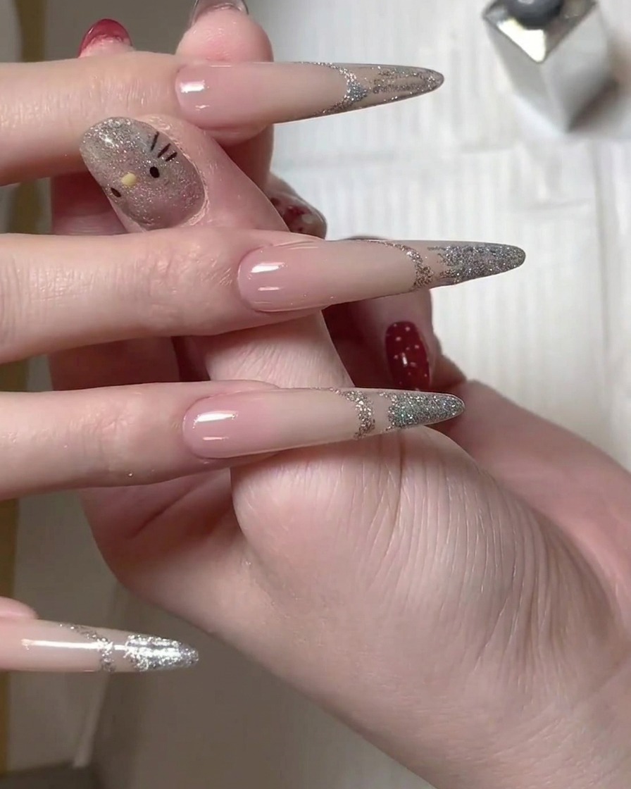Ein Pinsel trägt silbernes Glitzer-Gel auf die Spitze eines langen Nagels auf, um das French-Design zu erstellen.