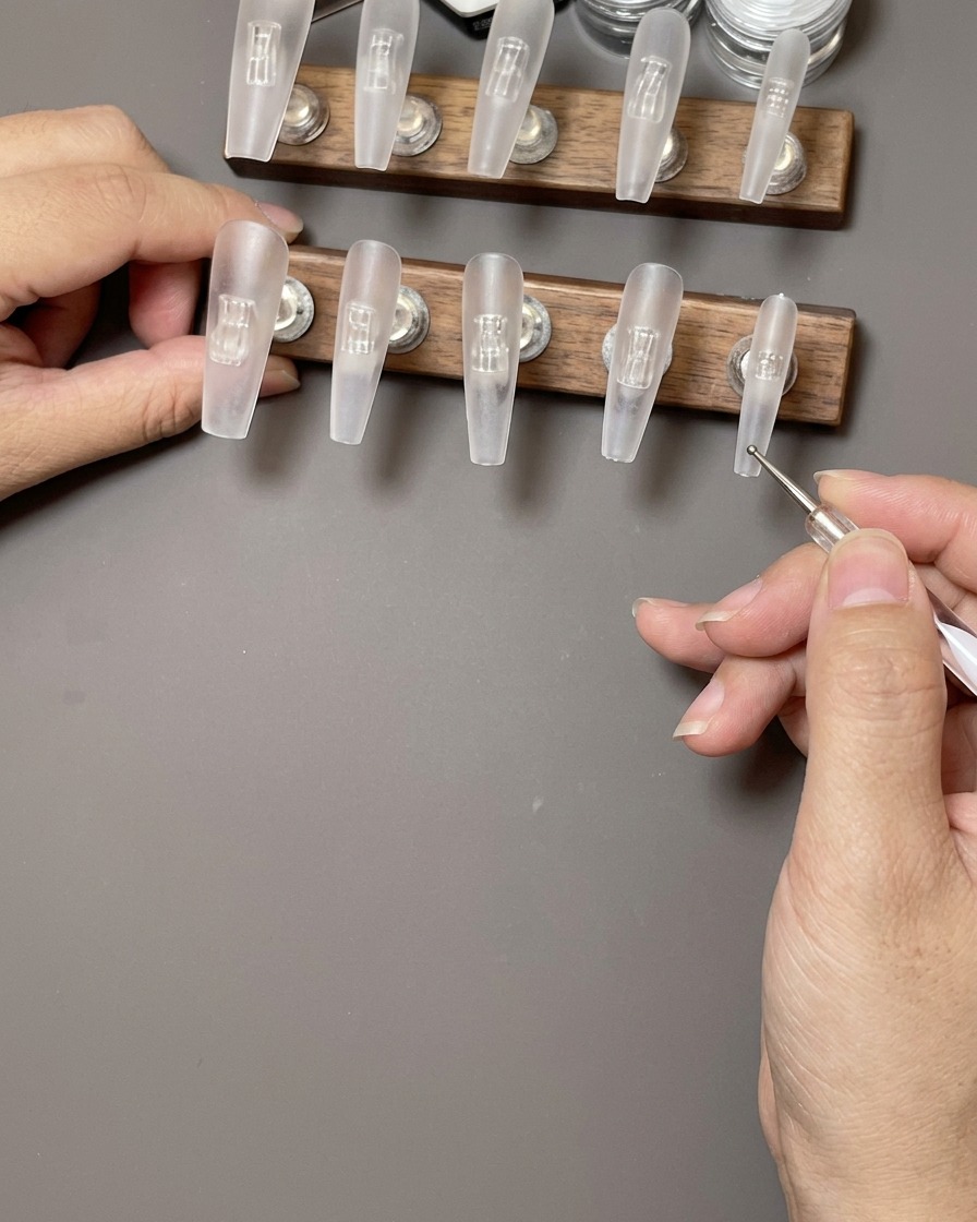 Eine Hand reinigt die Oberfläche eines klaren Press-On-Nagels mit einem fusselfreien Tuch.