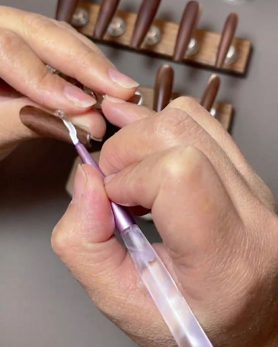 Nahaufnahme eines braunen Nagels, der mit einem weißen French-Tip-Design akzentuiert wird, das mit einem dünnen Nailart-Pinsel aufgetragen wird.