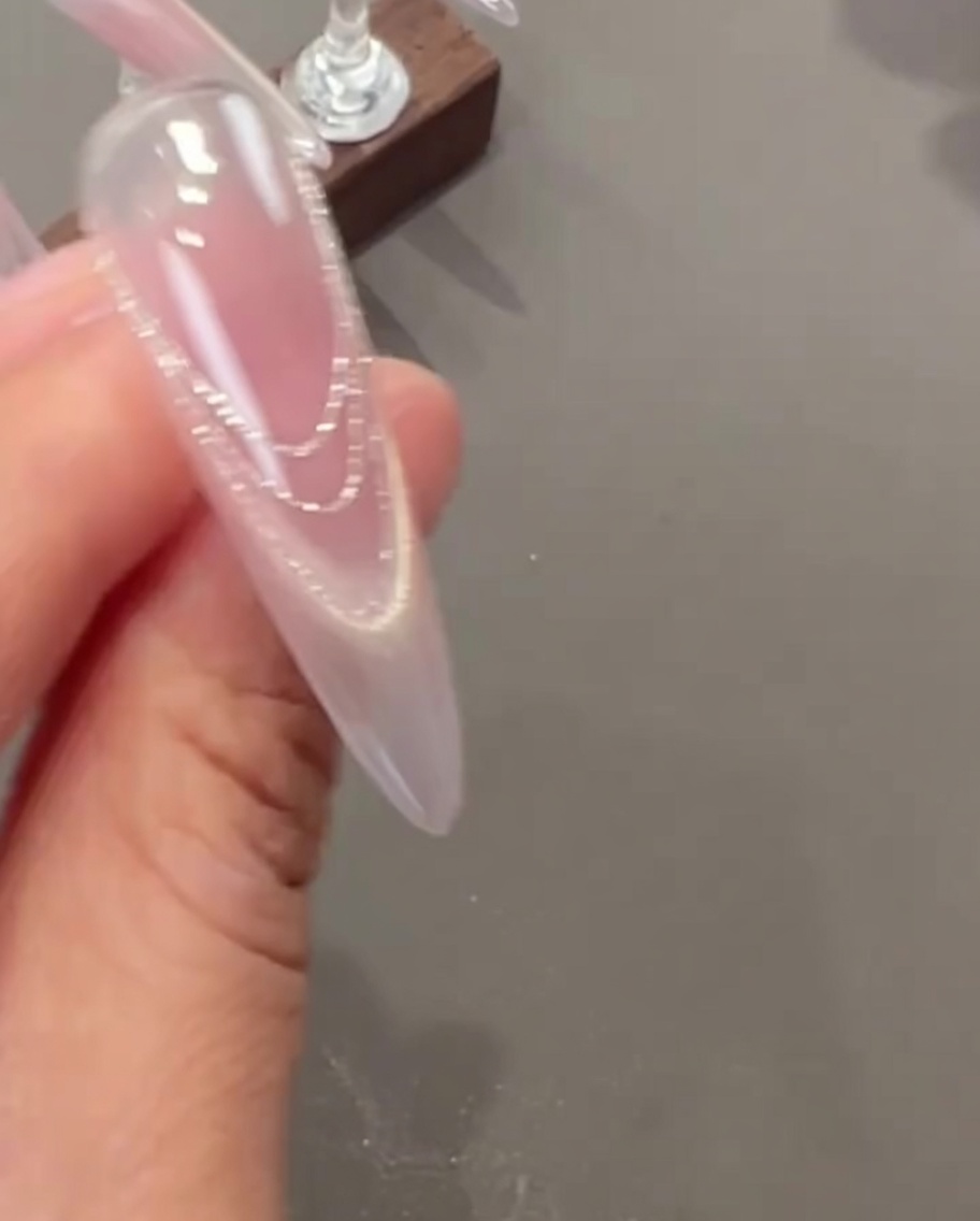 Eine Pinzette platziert kleine, filigrane Trockenblumen und winzige Perlen-Charms auf einem Fingernagel.