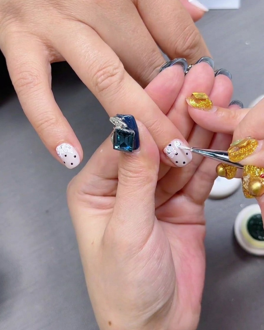 Ein glänzender Top Coat wird über die Nägel mit schwarzen Punkten aufgetragen.