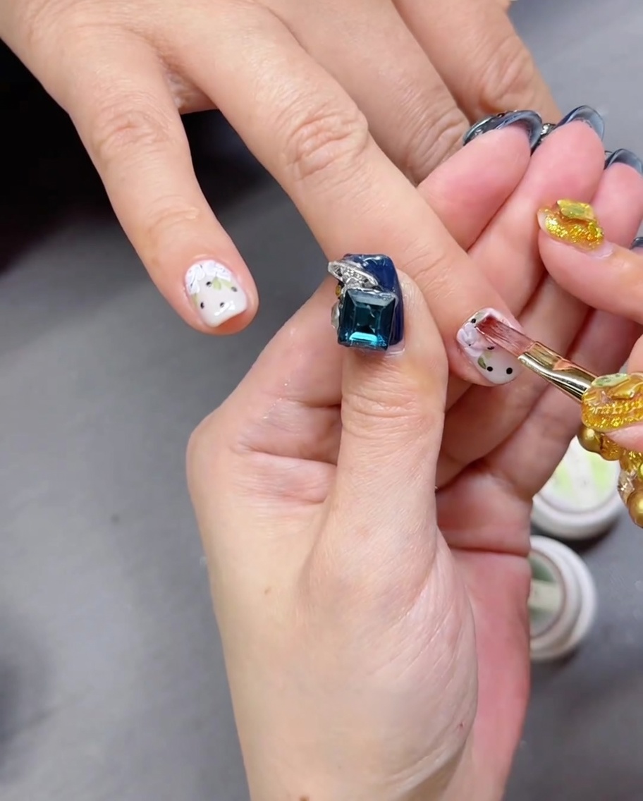 Ein Pinsel trägt klaren, glänzenden Top Coat über eine handgemalte Rosen- und Punktnagelkunst auf.