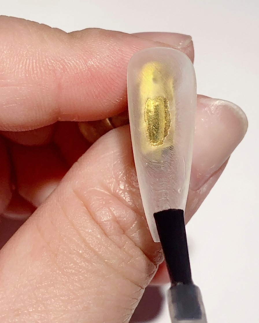 Ein Pinsel trägt eine dünne Schicht klares Basis-Gel auf die Innenseite einer transparenten Nagelspitze auf.