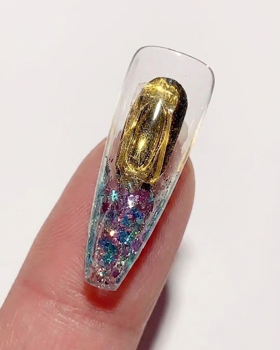 Auftragen eines klaren, dicken Hart-Nagelklebers über die goldfarbene Innenseite einer Nagelspitze.