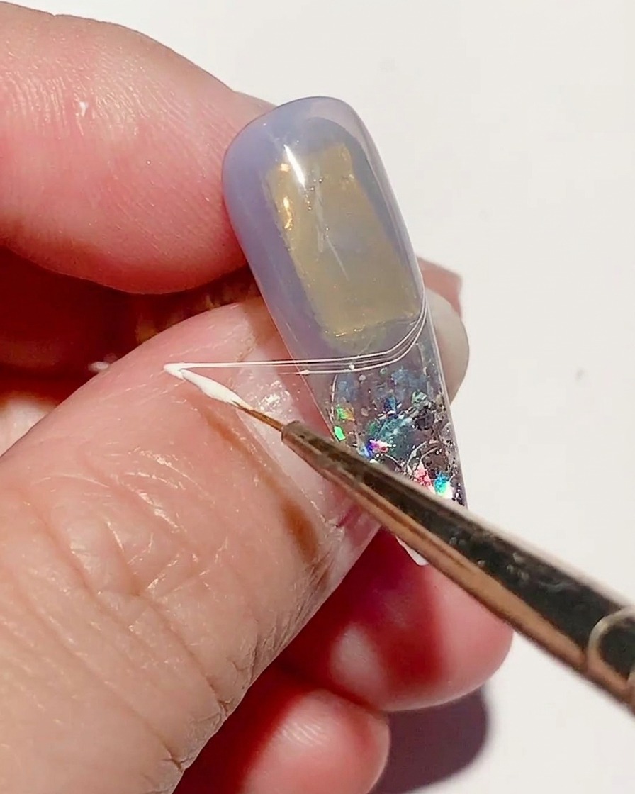 Ein feiner Liner-Pinsel zieht weißes Spider-Gel über die Nageloberfläche, um dünne, netzartige Linien zu erzeugen.