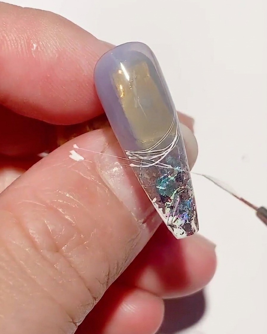 Eine Nahaufnahme eines Nagels mit weißen Spider-Gel-Linien, die unter einer UV-Nagellampe aushärten.