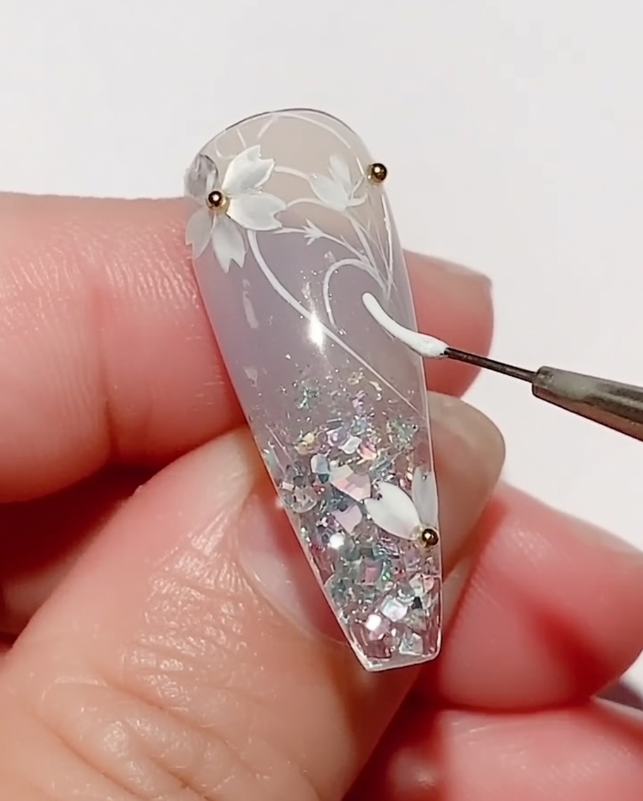 Ein dünner Liner-Pinsel trägt weißes Farbgel auf, um eine Blattform auf einen mit Kirschblüten verzierten Nagel zu zeichnen.