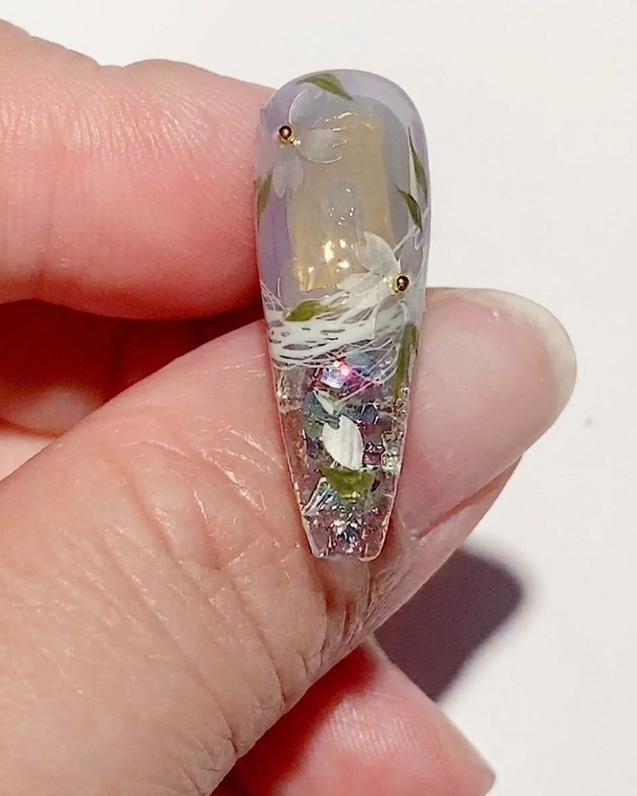 Ein manikürter Nagel mit Kirschblüten-Kunst, bei dem ein glänzender Top Coat über das gesamte Design aufgetragen wird.