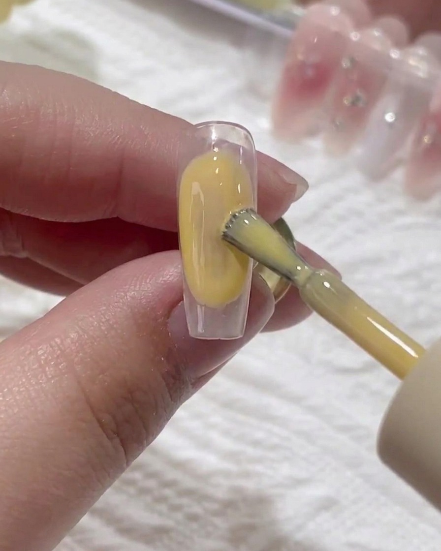 Ein Pinsel trägt eine dünne Schicht klaren Base-Gels auf einen vorbereiteten Naturnagel auf.