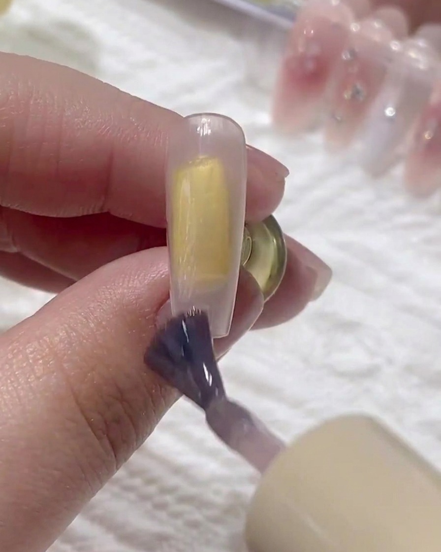 Ein Pinsel trägt eine zweite Schicht Base-Gel über die vorherige Schicht auf dem Nagel auf.