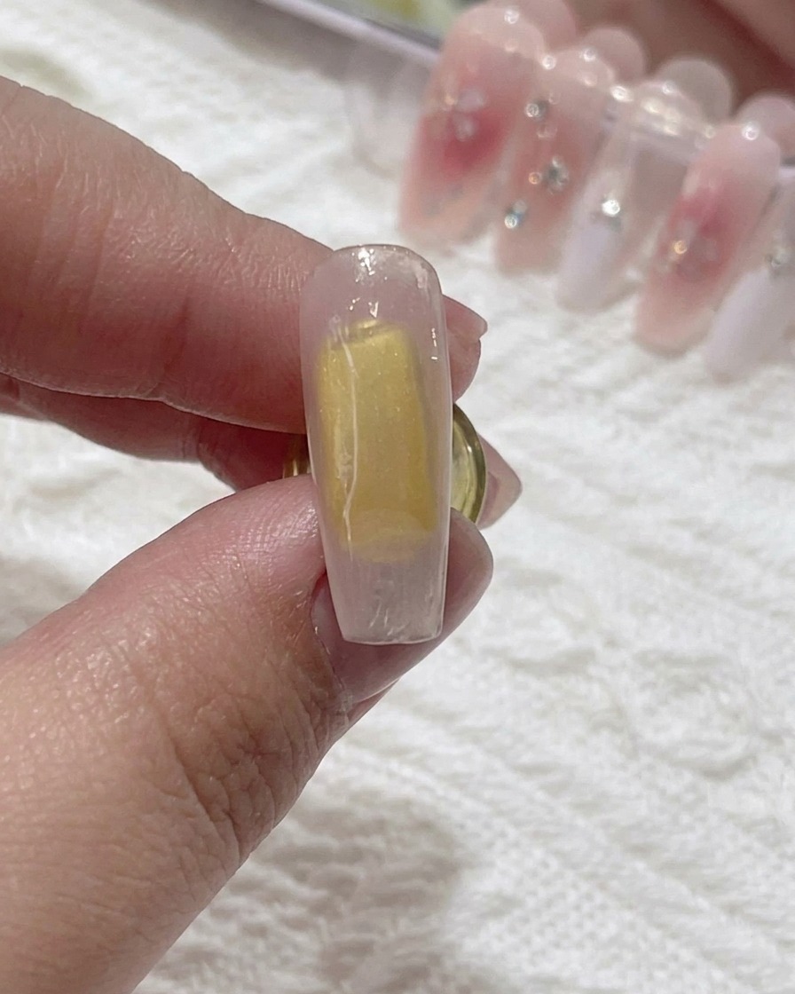 Ein Pinsel trägt klares Blooming-Gel auf die Nageloberfläche auf.