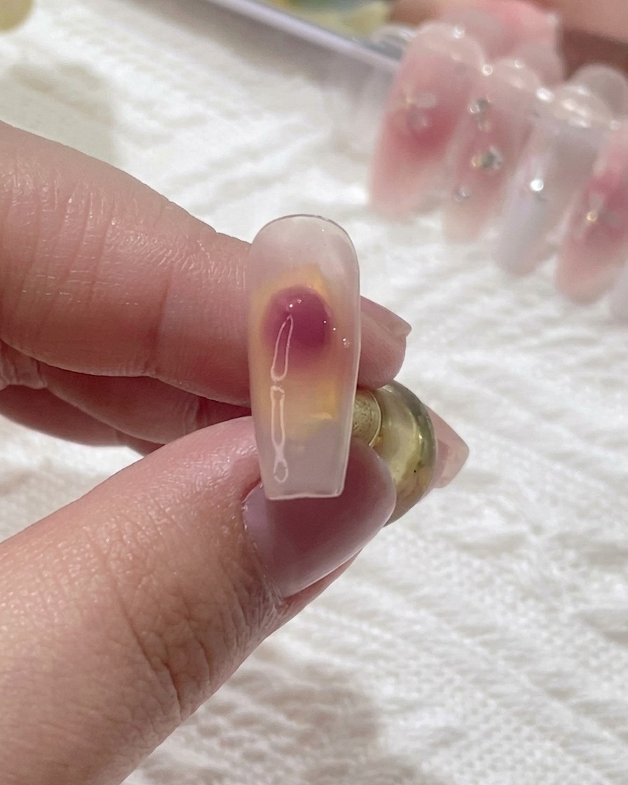 Nahaufnahme eines Nagelpinsels, der einen rosa Geltupfer auf einem klaren Nagel zu einem sanften Blush-Verlauf verblendet.