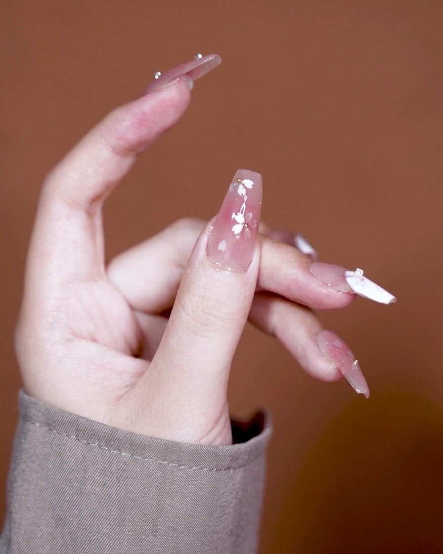 Ein Pinsel trägt ein klares, dickflüssiges Klebegel auf einen Nagel mit rosa Gradient-Basis auf.