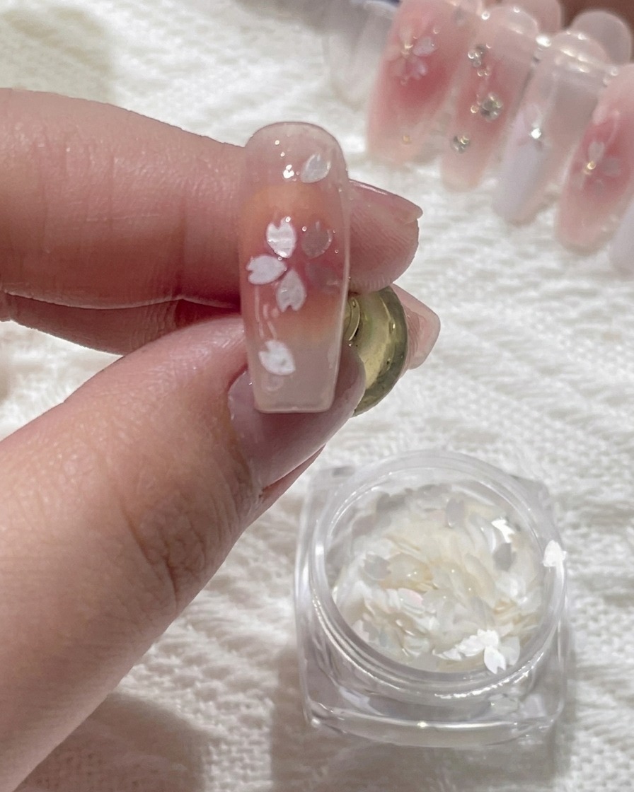 Ein Präzisionswerkzeug trägt einen winzigen Tropfen klaren Klebers in die Mitte eines floralen Nageldesigns auf.