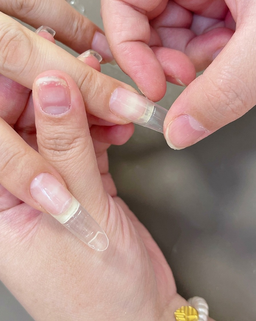 Finger drücken einen klaren Gel-Tip fest auf das Nagelbett, um eine korrekte Haftung zu gewährleisten.