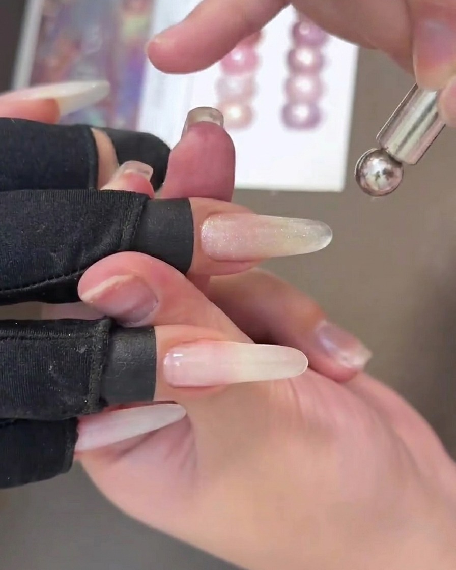 Nahaufnahme eines Nagels mit feuchtem Cat-Eye-Gel, bei dem ein metallischer Streifen mit einem Magnet-Tool mittig gezogen wird.