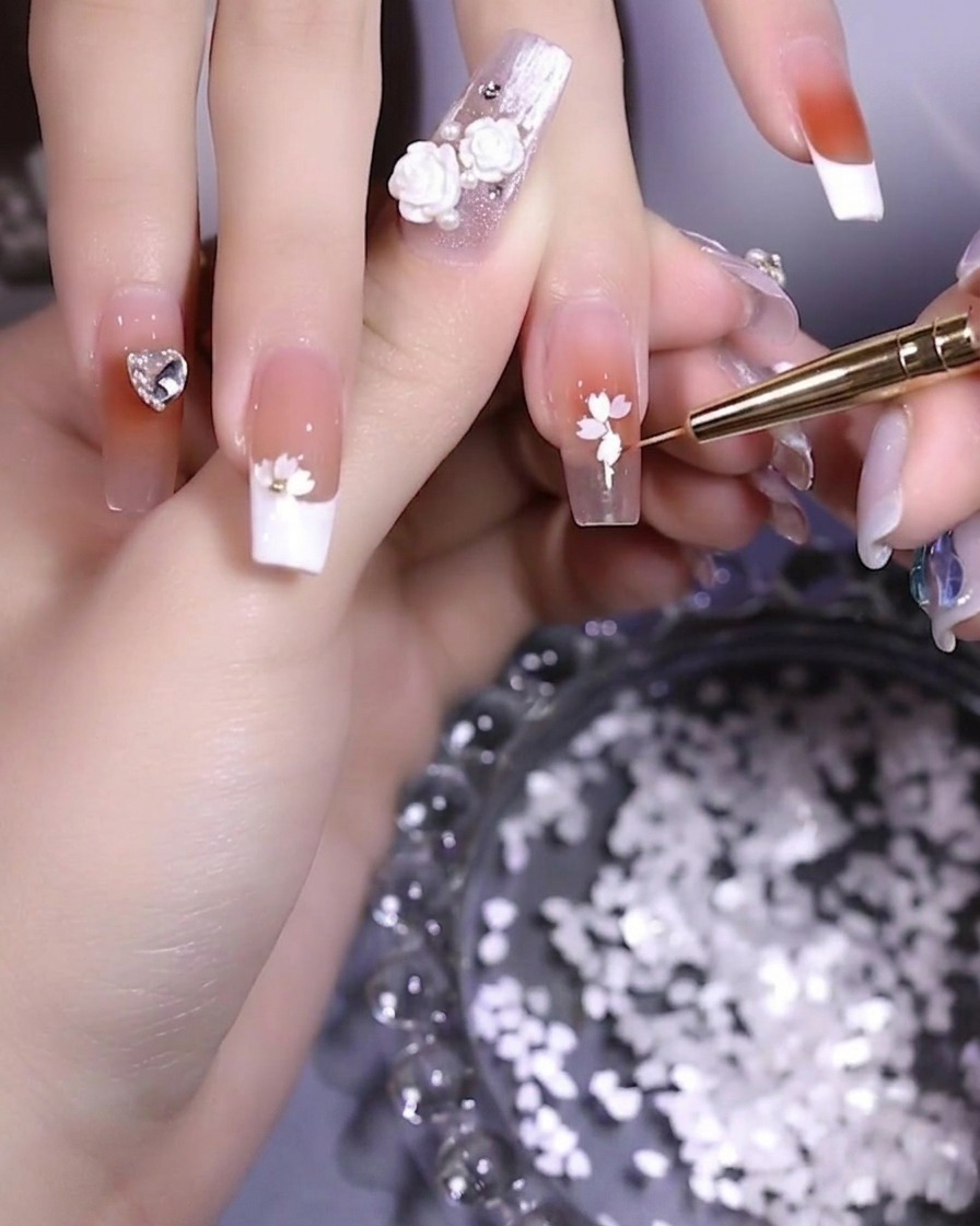 Nahaufnahme eines Nagels, bei dem Blütenblätter mit einer Pinzette zu einer Blumenform angeordnet werden.