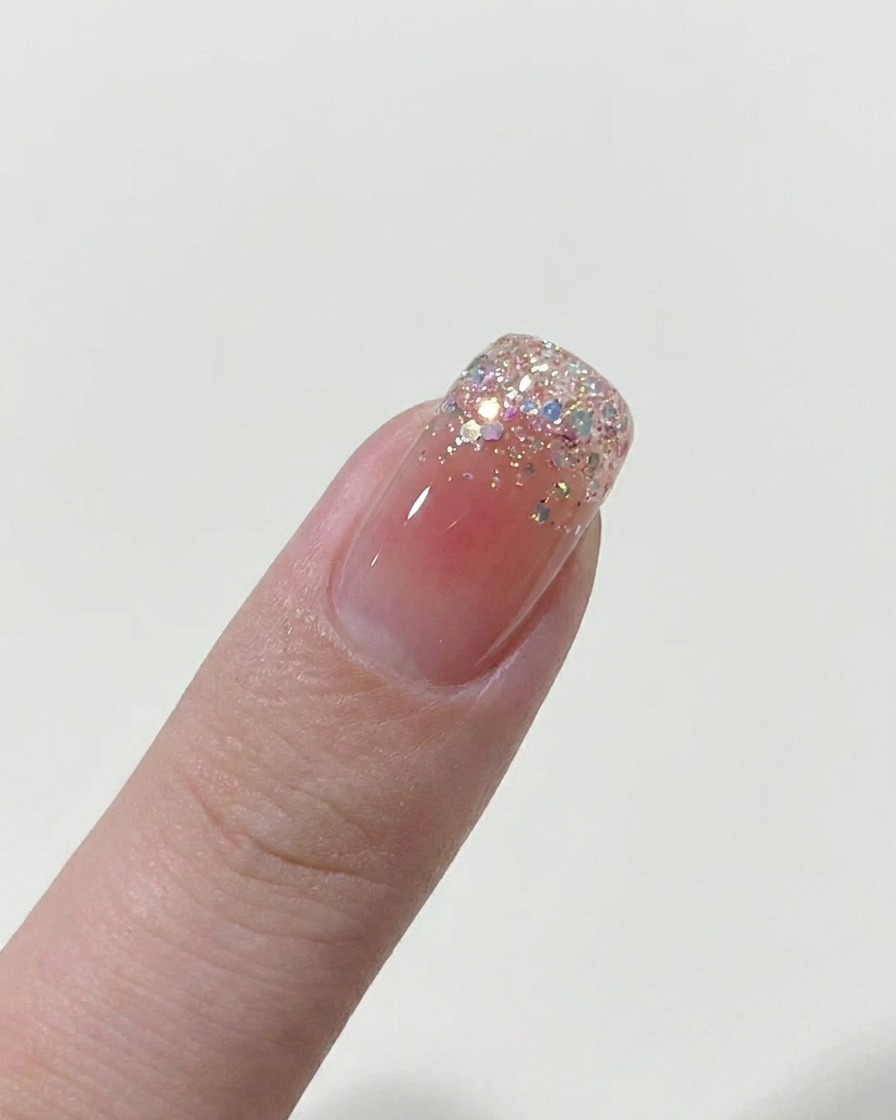 Ein Pinsel trägt eine dünne Schicht nudefarbenen Gellacks auf den Nagel auf.
