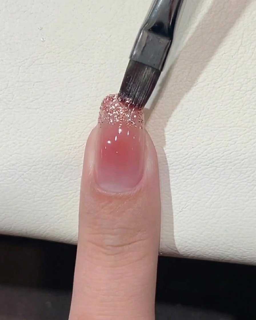 Ein Pinsel trägt groben Glitzer-Gellack auf die freie Nagelspitze auf.