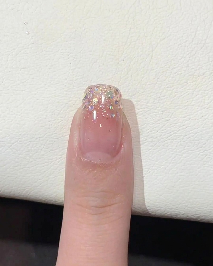 Ein Pinsel trägt klaren, glänzenden Top Coat über die Glitzer-Ombré-Spitze auf.