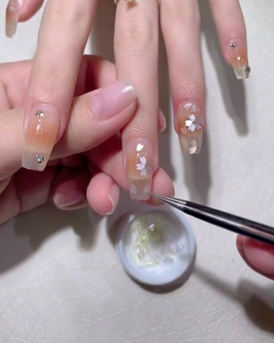 Nahaufnahme eines Nagels, bei dem Blüten-Applikationen mit einem feinen Pinsel und braunem Gel akzentuiert werden.