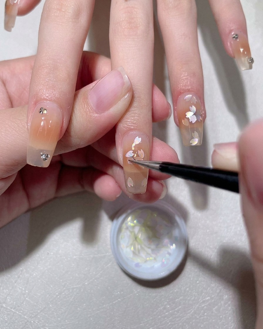 Ein Pinsel trägt eine milchig-weiße Gel-Basisschicht auf einen natürlichen Fingernagel auf.