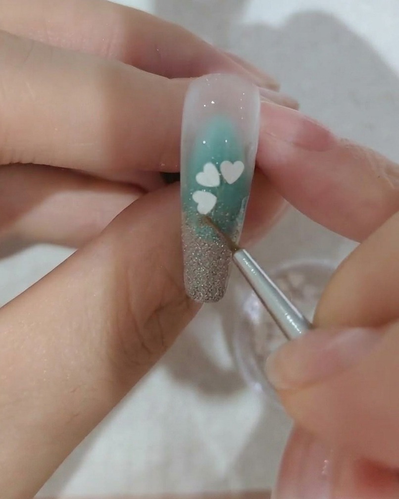 Nahaufnahme eines Nagels, der mit einem dritten weißen Kirschblüten-Paillettenblatt verziert wird.