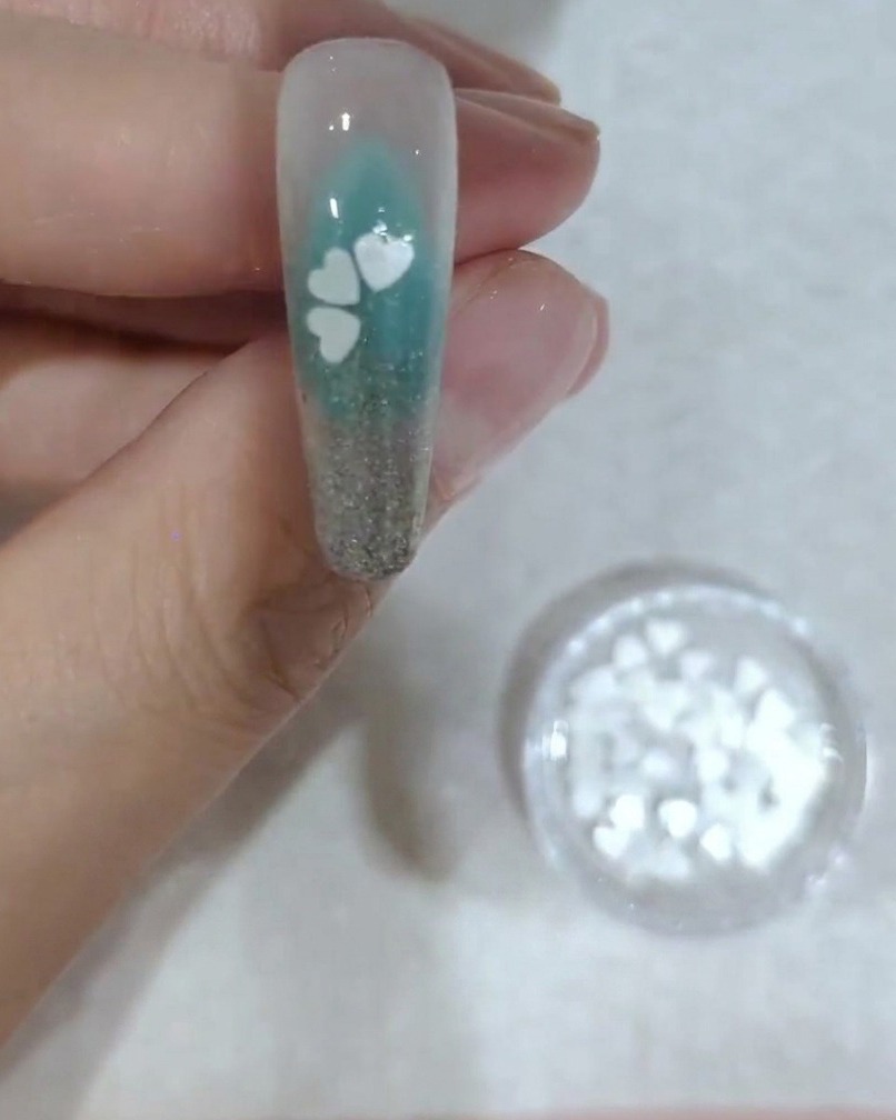 Nahaufnahme eines Nagels, der die Platzierung des vierten weißen Kirschblüten-Paillettenblatts zeigt.