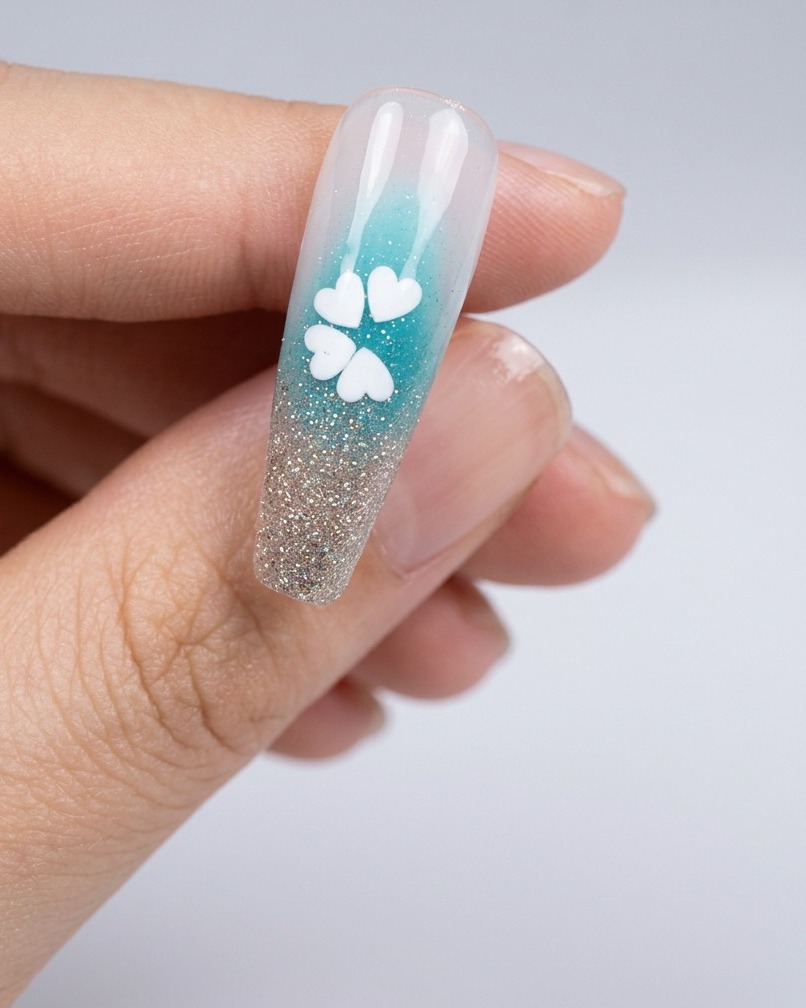 Nahaufnahme eines Nagels mit einem winzigen Klebepunkt in der Mitte der weißen Paillettenblüte.