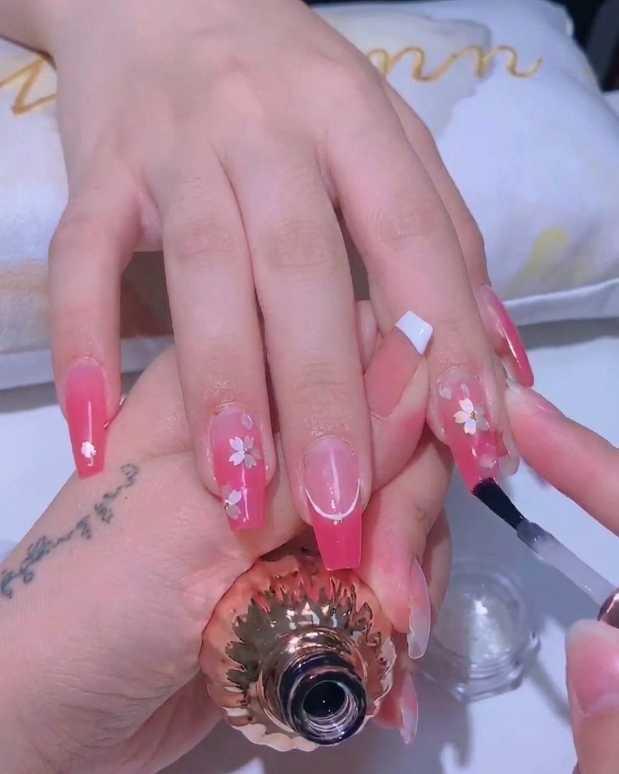 Ein Nagelpinsel trägt eine dünne, glänzende Versiegelung auf ein Kirschblüten-Design auf.
